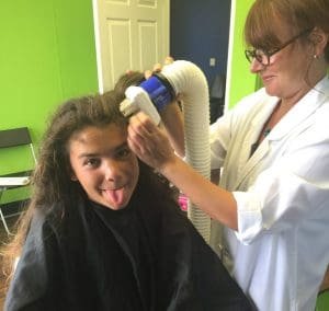 Technician performing heated air head lice treatment on cute girl sticking out her tongue