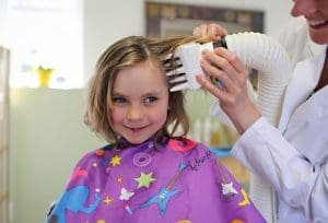 Technician performing heated air head lice treatment on smiling blond child