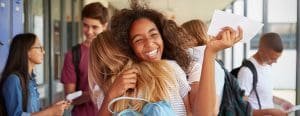 Friends give a happy hug at school with backpacks on and paper in hand