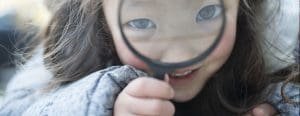 Little girl looking at the camera with a magnifying glass in front of her face
