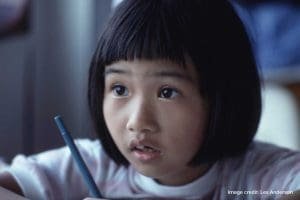 Little girl writing with a pen and looking up surprised
