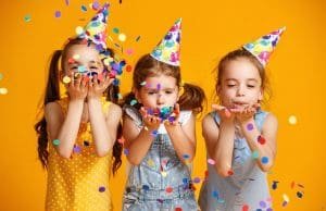 Three girls with party hats blowing confetti off their hands