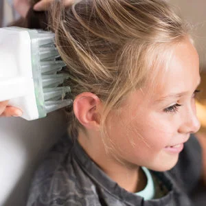 blond child receiving a heated0air treatment to cure her head lice
