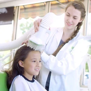 Technician performing heated air head lice treatment on child