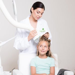 Technician performing heated air head lice treatment on blond child